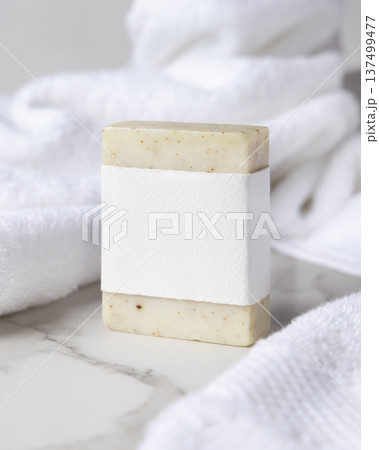 Mockup of beige solid soap bar with blank paper label near white bath towel, personal care packaging Mockup of beige solid soap bar with blank paper label near white bath towel, personal care packaging 137499477