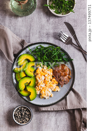 Fried eggs and bacon, fresh avocado and arugula on a plate on the table top and vertical view Fried eggs and bacon, fresh avocado and arugula on a plate on the table top and vertical view 137499751
