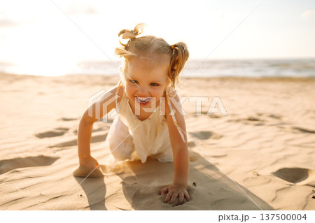 Young girl joyfully plays on the sandy beach during sunset, enjoying a carefree moment by the ocean Young girl joyfully plays on the sandy beach during sunset, enjoying a carefree moment by the ocean 137500004