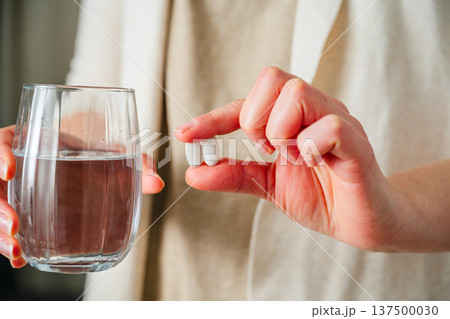 Woman holding two capsules pills in one hand and a glass with water, in other. Prescription medication, treatment sickness, seasonal cold flu concept Woman holding two capsules pills in one hand and a glass with water, in other. Prescription medication, treatment sickness, seasonal cold flu concept 137500030