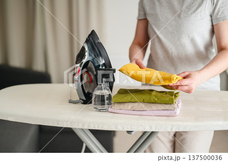 Ironing clothes. Woman ironing t-shirts at home. Daily chores. Laundry day. Gender roles. Ironing clothes. Woman ironing t-shirts at home. Daily chores. Laundry day. Gender roles. 137500036