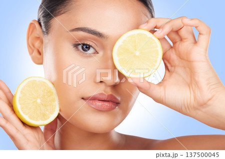 Lemon, portrait and beauty of woman in studio for vitamin c cosmetics, natural diet and detox. Face of model, healthy skincare and citrus fruits on eyes for sustainable dermatology on blue background 137500045