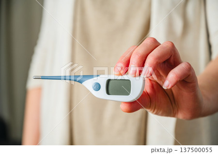 Electronic thermometer in female hands. Woman holding a digital thermometer. Flu and cold concept. Seasonal viruses Electronic thermometer in female hands. Woman holding a digital thermometer. Flu and cold concept. Seasonal viruses 137500055