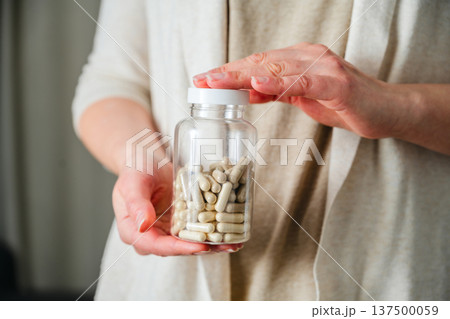 Woman holding a bottle with capsules pills. Prescription medication, treatment sickness, seasonal cold flu concept Woman holding a bottle with capsules pills. Prescription medication, treatment sickness, seasonal cold flu concept 137500059