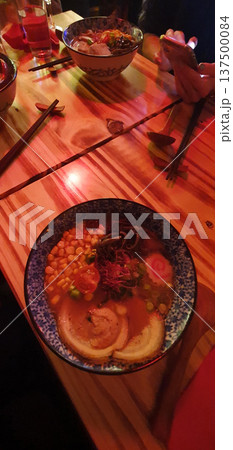 Phone photo of a ramen bowl in a low light Japanese style restaurant during lunch with friends. Casual dining scene showing social eating, comfort food, and everyday urban lifestyle. 137500084