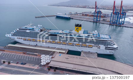 Majestic cruise ship anchored at bustling Port of Malaga, framed by industrial cranes and vibrant harbor life, showcasing maritime travel and port activity. 137500197