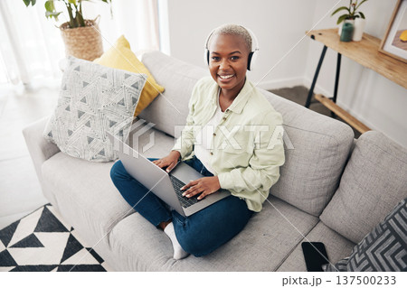 Portrait of black woman, remote work or laptop on sofa in living room for online research in headphones. Happy, top view or journalist working on computer for streaming or social media blog at home Portrait of black woman, remote work or laptop on sofa in living room for online research in headphones. Happy, top view or journalist working on computer for streaming or social media blog at home 137500233