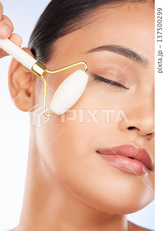 Woman, face roller and massage in studio for skincare, grooming and aesthetic dermatology on white background. Model, crystal cosmetics and facial beauty tools for lymphatic drainage, shine and glow Woman, face roller and massage in studio for skincare, grooming and aesthetic dermatology on white background. Model, crystal cosmetics and facial beauty tools for lymphatic drainage, shine and glow 137500299