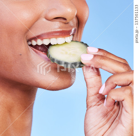 Woman, mouth and bite on cucumber in diet, natural nutrition or detox against a blue studio background. Closeup of female person eating organic vegetable in healthy wellness, dermatology or beauty Woman, mouth and bite on cucumber in diet, natural nutrition or detox against a blue studio background. Closeup of female person eating organic vegetable in healthy wellness, dermatology or beauty 137501133
