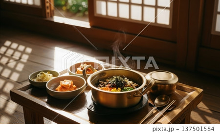 Traditional Korean bibimbap meal with kimchi banchan side dishes served in stone bowl on wooden table in hanok house with natural sunlight streaming through lattice windows 137501584