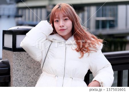 冬の川辺で微笑む女性モデル。白いアウターと都会の風景が調和する爽やかなポートレート。 137501601