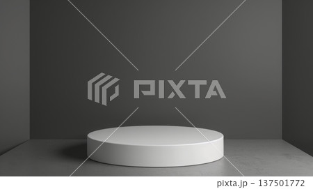 A white cylindrical pedestal stands centrally in a minimalist, gray-walled room with a matching gray floor, lit softly from above. 137501772