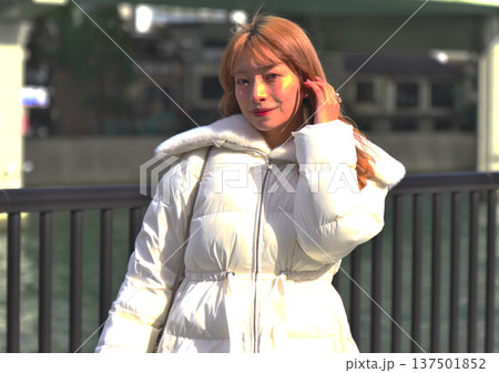 冬の都会の川辺で振り返る女性モデル。白いアウターとリバーサイドの風景が映えるポートレート。 137501852