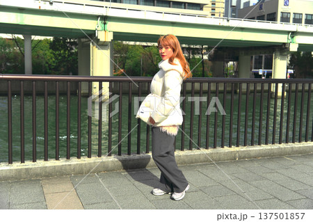 冬の都会の川辺で振り返る女性モデル。白いアウターとリバーサイドの風景が映えるポートレート。 冬の都会の川辺で振り返る女性モデル。白いアウターとリバーサイドの風景が映えるポートレート。 137501857