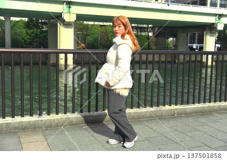 冬の都会の川辺で振り返る女性モデル。白いアウターとリバーサイドの風景が映えるポートレート。 冬の都会の川辺で振り返る女性モデル。白いアウターとリバーサイドの風景が映えるポートレート。 137501858