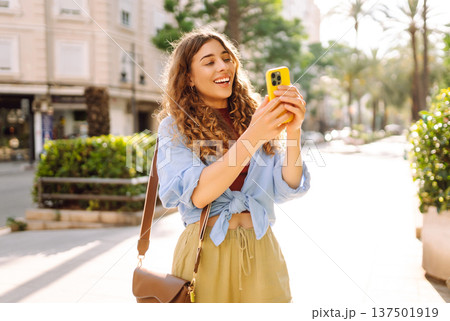 Smiling woman walking around old street using smartphone. Communication, social networks concept. 137501919