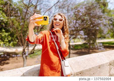 Young woman taking a cheerful selfie in blooming park on a sunny day. Joy concept. Active lifestyle. Young woman taking a cheerful selfie in blooming park on a sunny day. Joy concept. Active lifestyle. 137502004