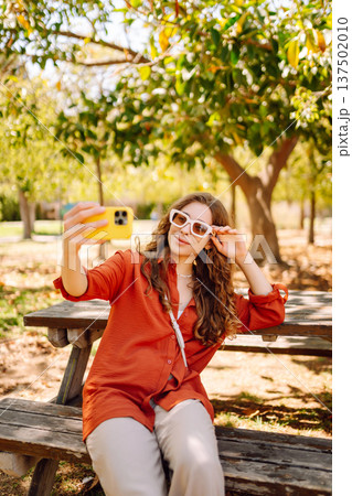 Young woman enjoying sunny day taking selfie in busy park. Blogging concept, weekend. Lifestyle. Young woman enjoying sunny day taking selfie in busy park. Blogging concept, weekend. Lifestyle. 137502010