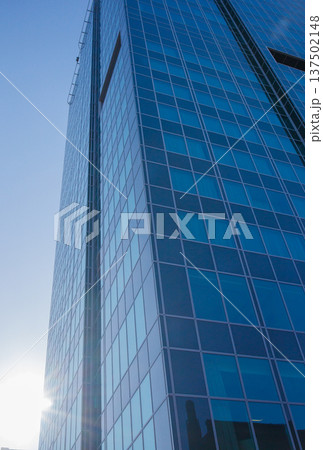 City skyscraper building exterior facade with blue sky background and bright sun shining behind the building. Repetitive windows made of reflective glass. Big city life, contemporary architecture. City skyscraper building exterior facade with blue sky background and bright sun shining behind the building. Repetitive windows made of reflective glass. Big city life, contemporary architecture. 137502148