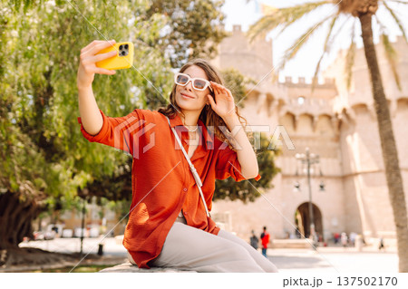 Cheerful woman taking a selfie in stylish sunglasses while strolling down a sunlit city street 137502170