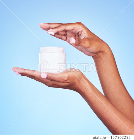 Skincare, cream and product with hands of woman in studio for beauty, facial or moisturizer. Spa treatment, health and collagen with closeup of person on blue background for lotion and sunscreen 137502253