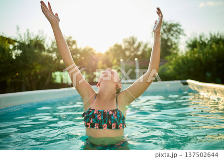 Teen girl enjoying a summer day in a pool, celebrating with arms raised under the warm sun 137502644