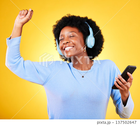 Happy black woman, phone and headphones listening to music against a yellow studio background. African female person smile, afro or mobile smartphone app dancing to audio track, sound or podcast 137502647