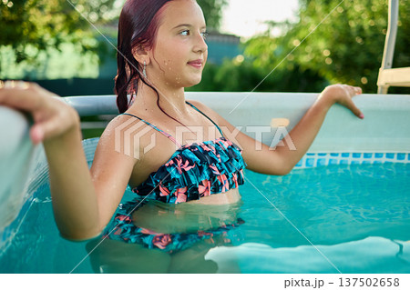 Teen girl enjoying a summer afternoon in a backyard pool surrounded by lush greenery and sunshine 137502658