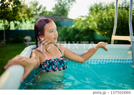 Teen girl enjoying a summer afternoon in a backyard pool surrounded by lush greenery and sunshine 137502660
