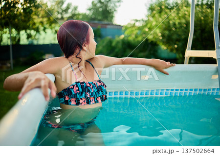 Teen girl enjoying a summer afternoon in a backyard pool surrounded by lush greenery and sunshine 137502664