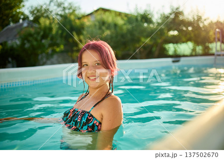Teen girl enjoying a refreshing swim in a backyard pool during a sunny summer day 137502670