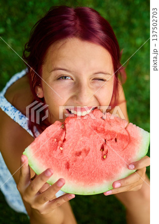 Teen girl enjoying a slice of watermelon in a sunny green park during summer afternoon 137502703