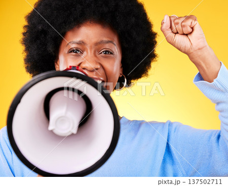 Black woman, portrait and megaphone with fist in protest, fight or march against a yellow studio background. African female person or activist with noise, bullhorn or loudspeaker in voice or justice 137502711