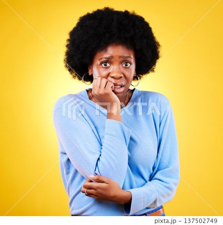 Biting nails, anxiety and a scared woman in studio for fear, mental health or nervous behaviour. Portrait of African person on yellow background worried, stress or panic for phobia, terror or horror 137502749