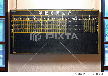 古い木造校舎の壁に掲げられた手書き文字が残る学級時間割表の黒板 137503310