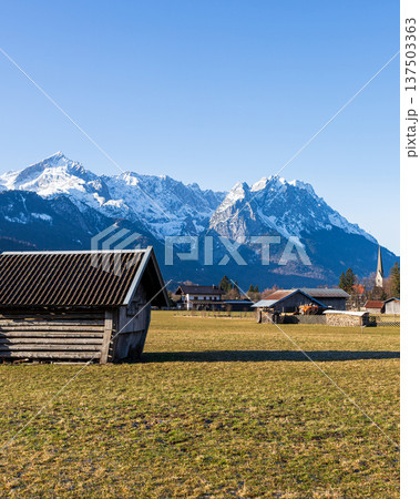 Traditional wooden hut in Bavarian countryside with snow capped Alps mountains and clear blue sky 137503363