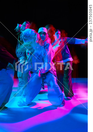 Hip hop dancers performing synchronized street dance under colorful neon lighting with motion blur 137503845