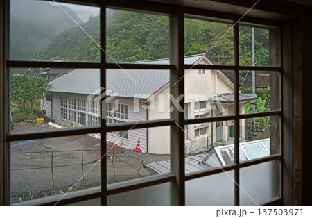 雨の日の窓越しに望む霧深い山里に佇む木造校舎の体育館 雨の日の窓越しに望む霧深い山里に佇む木造校舎の体育館 137503971