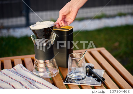 Specialty pour over coffee setup with hand placing paper filter outdoors 137504468