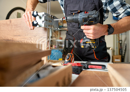 Carpenter drilling wooden board with cordless drill and drilling jig 137504505