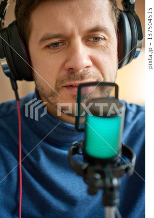 Man Wearing Headphones Speaking into Microphone with Pop Filter Man Wearing Headphones Speaking into Microphone with Pop Filter 137504515