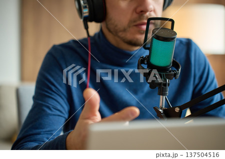 Man speaking into podcast microphone with headphones at desk Man speaking into podcast microphone with headphones at desk 137504516