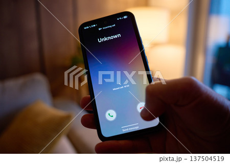 Hand holding smartphone showing unknown incoming call on screen 137504519