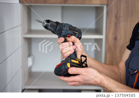 Close-up of handyman holding cordless drill during kitchen cabinet installation Close-up of handyman holding cordless drill during kitchen cabinet installation 137504585