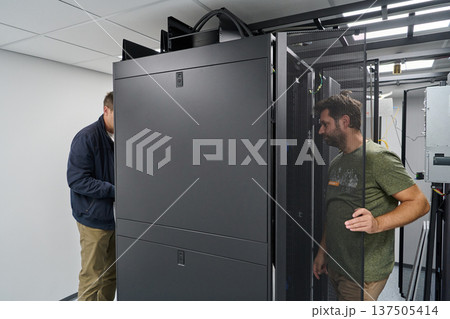Two technicians installing and inspecting servers in a modern data center rack room for network infrastructure 137505414