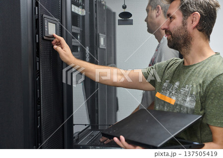 It technician checking server rack control panel in data center with laptop 137505419