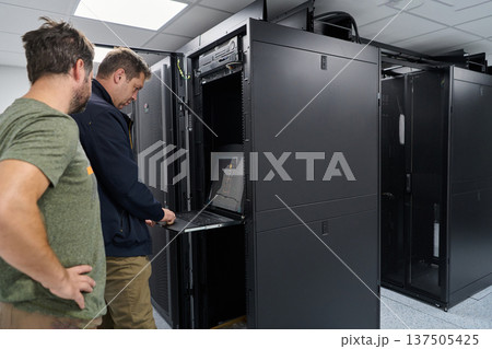 Two IT technicians working on server rack in a data center performing maintenance and system checks 137505425