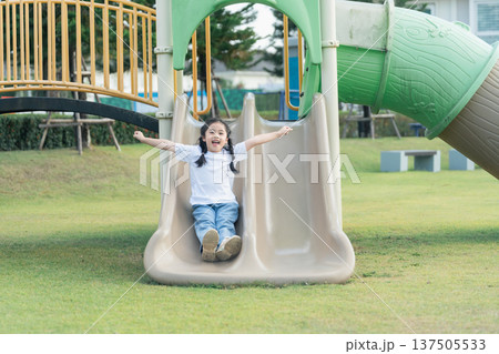 Joyful child sliding down a playground slide with excitement, capturing the essence of childhood fun, freedom, and outdoor play in a serene park setting 137505533