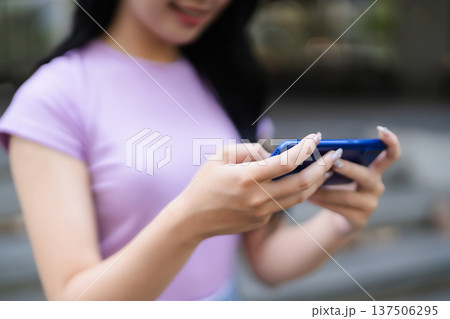 Asian adult woman hands hold modern blue smartphone playing mobile game or texting social media apps outdoor urban street digital lifestyle 137506295