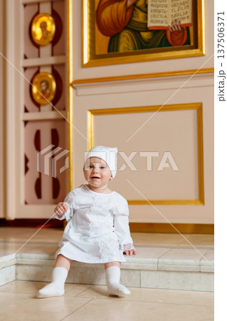 Child in white dress sitting inside a church 137506371